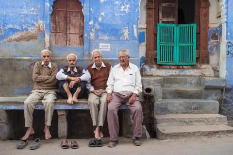 Travel: Four elderly men sitting on stone bench on street in front of a traditional blue house in Jodhpur, India.