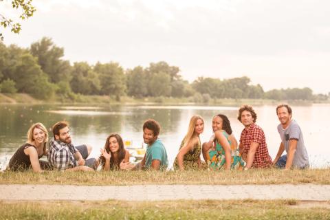 Lifestyle: 8 young good looking multi-cultural adults laying on grass close to lake in summerly feel.
