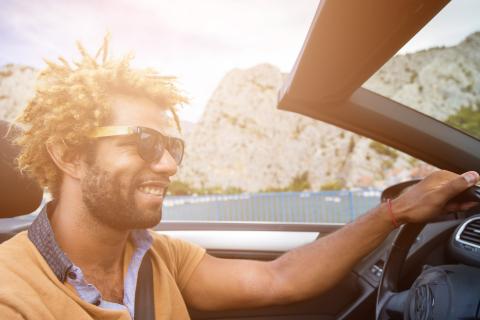 Lifestyle: Young happy man with summer dread locks and sunglasses in convertible sports car.