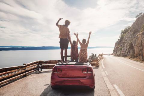 Lifestyle: Group of happy young adults standing in red convertible sports car along the coastal road of Makarska in Croatia.