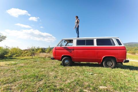 Lifestyle: Woman standing on her travelling red van in the countryside.