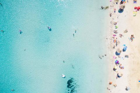 Aerial: View of sandy beach with tourists swimming in beautiful clear sea water