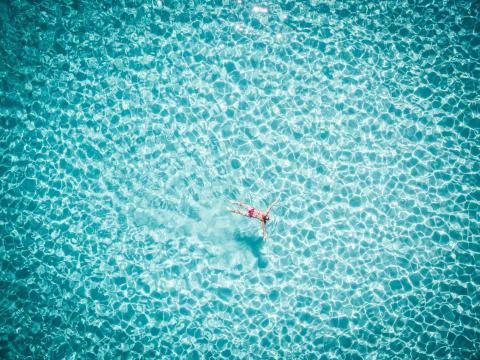Aerial: Beautiful young woman swimming in transparent rippled sea.