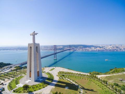 Aerial: View of Sanctuary of Christ the King overlooking Lisbon and 25 de Abril Bridge connecting Lisbon and Almada, Portugal.